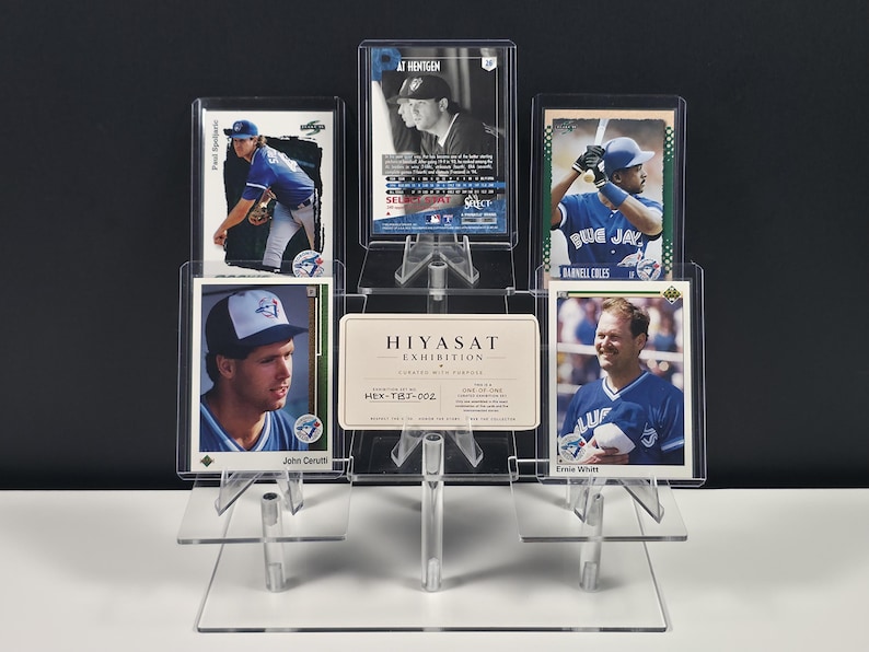May include: A clear acrylic tiered display stand holding five baseball trading cards and a rectangular white card with the text HIYASAT EXHIBITION CURATED WITH PURPOSE HEX-TBJ-002 ONE-OF-ONE. The stand features multiple levels to showcase the cards.