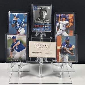 May include: A clear acrylic tiered display stand holding five baseball trading cards and a rectangular white card with the text HIYASAT EXHIBITION CURATED WITH PURPOSE HEX-TBJ-001 ONE OF ONE. The cards feature various baseball players in blue uniforms.