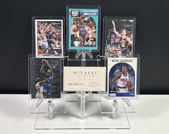 Könnte beinhalten: Ein transparenter, abgestufter Acryl-Displayständer mit vier Basketball-Sammelkarten und einer zentralen, rechteckigen Hiyasat Exhibition-Karte. Die Karten zeigen verschiedene Spieler in Aktion, darunter Isiah Thomas und Kevin Johnson, in Schutzhüllen.