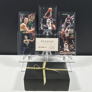 May include: A black gift box with a gold ribbon sits in front of a clear acrylic display stand holding five basketball trading cards and a white card with the text HIYASAT EXHIBITION HEX-NBA-001 printed in black ink.