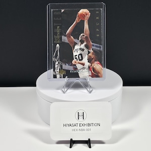 May include: A David Robinson basketball trading card in a protective plastic case, featuring the player in a white Spurs jersey with number 50, shooting a basketball. The card includes the text David Robinson and Electric Court.