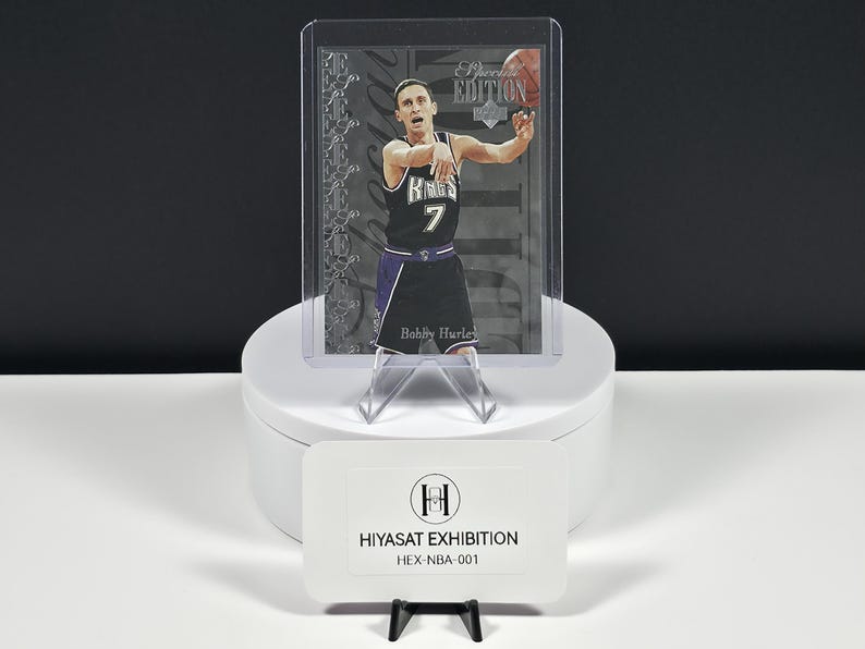 May include: A Bobby Hurley basketball trading card in a protective plastic sleeve, featuring the player in a black Kings jersey with the number 7. The card includes the text 'Special Edition' and is displayed with a Hiyasat Exhibition label.