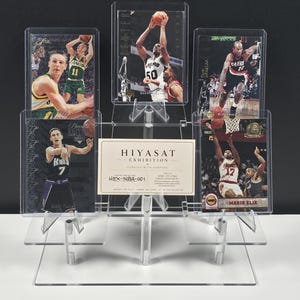 Op de afbeelding: Een doorzichtige, getrapte displaystandaard van acryl met vijf basketbal-verzamelkaarten en een centrale rechthoekige kaart met het label HIYASAT EXHIBITION CURATED WITH PURPOSE HEX-NBA-001. De kaarten tonen diverse spelers in actie.