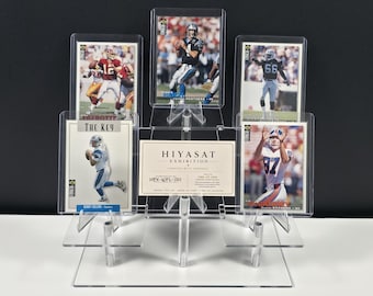 Könnte beinhalten: Ein transparenter, abgestufter Acryl-Präsentationsständer mit fünf Sport-Sammelkarten und einer zentralen rechteckigen Karte mit der Aufschrift HIYASAT EXHIBITION, HEX-NFL-001 und ONE-OF-ONE. Die Karten zeigen verschiedene Footballspieler in Aktion.