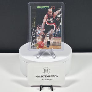 May include: A sports trading card featuring Clyde Drexler in a black and red Portland Trail Blazers uniform, dribbling a basketball on a court. The card is encased in a clear plastic protective sleeve and displays the text Clyde Drexler.