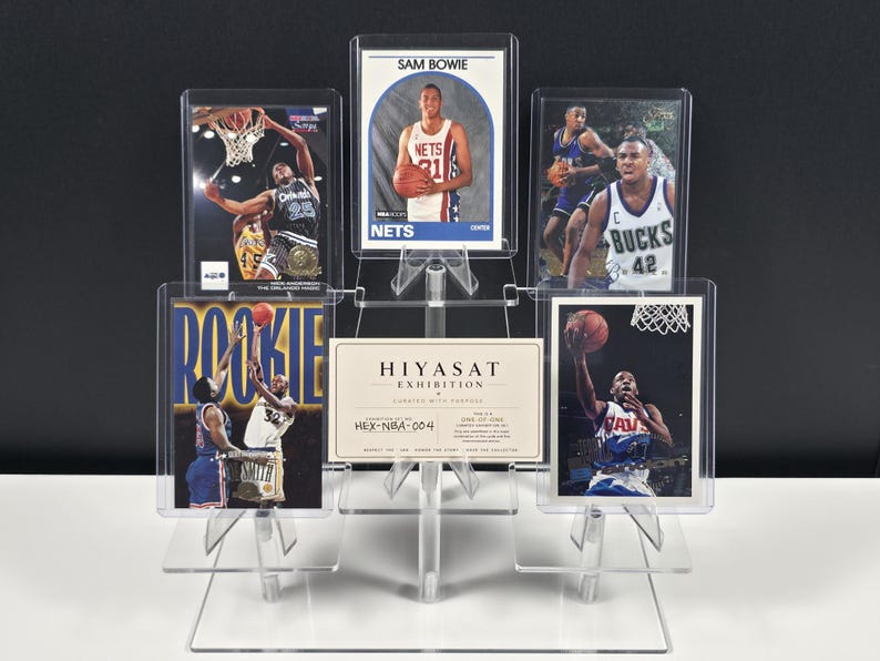 Op de afbeelding: Een doorzichtige, getrapte displaystandaard van acryl met vijf basketbal-verzamelkaarten en een centrale Hiyasat Exhibition-kaart. De kaarten tonen diverse spelers in actie, waaronder Sam Bowie, en zitten in beschermende plastic hoesjes.