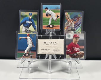 Könnte beinhalten: Ein transparenter, abgestufter Acryl-Displayständer mit vier Baseball-Sammelkarten und einer zentralen rechteckigen Karte mit der Aufschrift HIYASAT EXHIBITION CURATED WITH PURPOSE. Die Karten zeigen verschiedene Spieler in Action-Posen, darunter Jim Abbott und Jim Eisenreich.