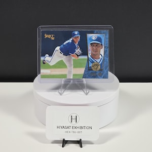Puede incluir: Una tarjeta de b&eacute;isbol Select 95 que muestra a un jugador con uniforme azul y blanco, dentro de un protector de pl&aacute;stico transparente. La tarjeta presenta una foto de acci&oacute;n de cuerpo completo y un retrato, con un emblema circular dorado y el texto HIYASAT EXHIBITION.