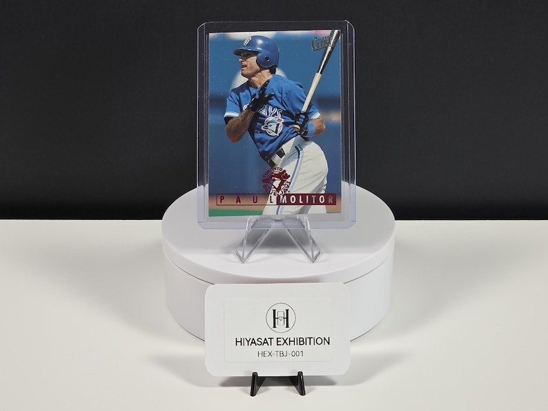 Puede incluir: Una tarjeta de b&eacute;isbol que muestra a Paul Molitor con un uniforme azul de los Toronto Blue Jays, sosteniendo un bate. La tarjeta est&aacute; dentro de una funda protectora de pl&aacute;stico transparente y muestra el nombre PAUL MOLITOR en una franja roja.