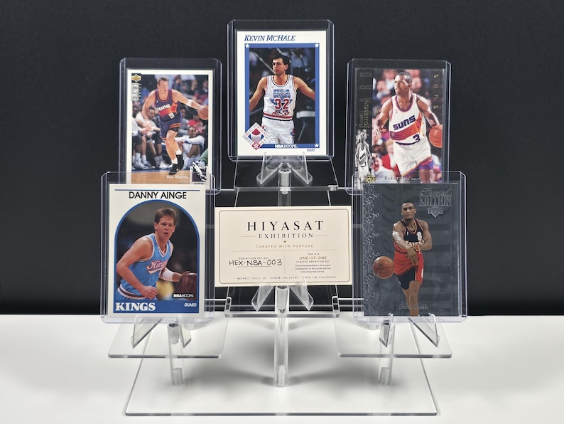 K&ouml;nnte beinhalten: Ein transparenter, gestufter Acryl-Displayst&auml;nder mit f&uuml;nf Basketball-Sammelkarten und einer zentralen rechteckigen Karte mit der Aufschrift HIYASAT EXHIBITION CURATED WITH PURPOSE HEX-NBA-003. Die Karten zeigen verschiedene Spieler in Aktion.