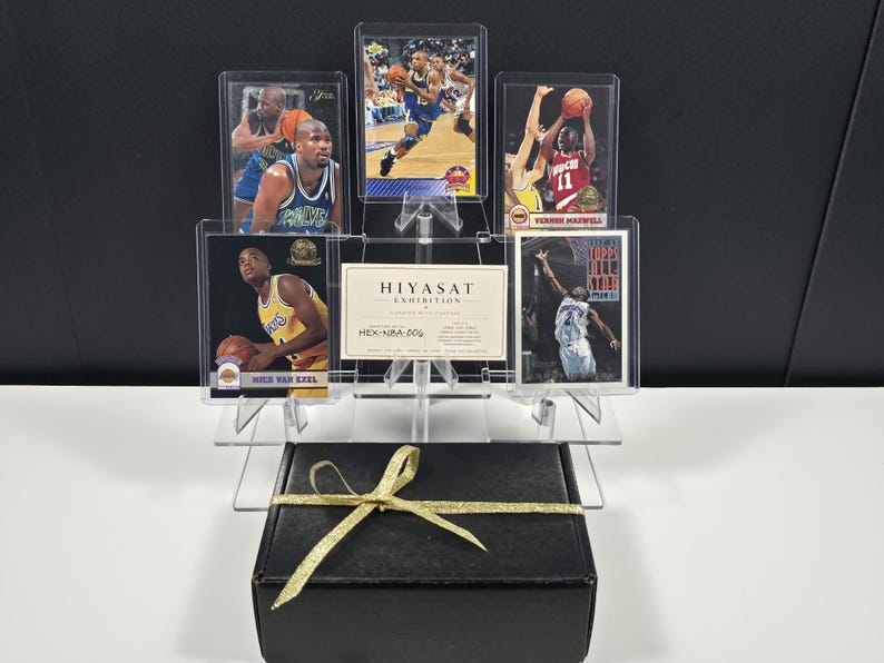 K&ouml;nnte beinhalten: Eine schwarze Geschenkbox mit goldenem Band steht unter einem transparenten Acryl-Displayst&auml;nder, der f&uuml;nf Basketball-Sammelkarten und eine rechteckige Karte mit der Aufschrift HIYASAT EXHIBITION HEX-NBA-006 enth&auml;lt. Die Karten zeigen verschiedene Spieler.