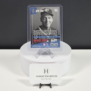 Puede incluir: Una tarjeta de b&eacute;isbol de David Cone en una funda protectora de pl&aacute;stico transparente. La tarjeta presenta un retrato en blanco y negro del jugador, texto azul y estad&iacute;sticas. Un letrero rectangular blanco con la etiqueta HIYASAT EXHIBITION HEX-TBJ-001 se encuentra debajo.