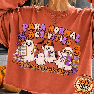 May include: A rust-colored crewneck sweatshirt featuring a graphic with the text "PARA NORMAL ACTIVITIES" and "paraprofessional". The design includes four ghosts, stacks of books, a clipboard, a pencil, and pumpkins in orange and purple.