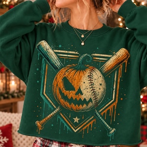 May include: A dark green long-sleeve sweatshirt featuring a graphic print of a jack-o'-lantern pumpkin merged with a baseball, positioned between two crossed baseball bats, all set against a geometric frame with dripping paint accents.