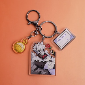 May include: A metal keychain featuring three acrylic charms: a yellow pocket watch, a character illustration of a white-haired wolf-like figure in a maid outfit holding a red rose, and a rectangular ID tag labeled VON LYCAON with text.