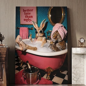 May include: A wall art print depicting a rabbit and a leopard in a pink clawfoot bathtub filled with bubbles. The rabbit wears sunglasses and pearls, while the leopard wears a pink towel. A sign reads better late than ugly in pink text.