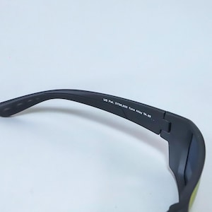 Puede incluir: Un par de gafas de sol negro mate con un dise&ntilde;o de montura curva. El interior de la patilla tiene impreso el texto US Pat. D706,858 Tuna Alley TA 03, que indica el modelo espec&iacute;fico y la informaci&oacute;n de patente de esta montura.