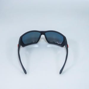 Puede incluir: Gafas de sol negras con montura de acabado mate y lentes oscuras y reflectantes. Las patillas presentan peque&ntilde;os detalles rectangulares de color rojo brillante cerca de las bisagras, lo que aporta un sutil contraste al dise&ntilde;o oscuro de las gafas.
