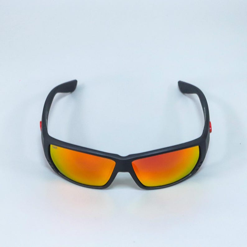 Puede incluir: Gafas de sol deportivas con montura negra mate y lentes reflectantes de color naranja rojizo. El dise&ntilde;o envolvente incluye peque&ntilde;os detalles rojos en las patillas exteriores, ofreciendo un aspecto elegante con un amplio campo de visi&oacute;n.