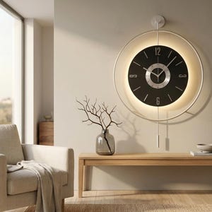 Könnte beinhalten: Eine große, kreisförmige Wanduhr mit schwarzem Zifferblatt und silbernen Ziffern auf der Zwölf- und Sechs-Uhr-Position, umgeben von einem dünnen weißen Rahmen mit integrierter Hintergrundbeleuchtung und einem vertikalen Pendel.