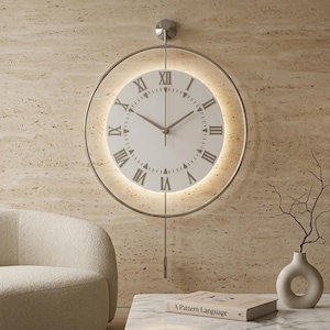 May include: A circular wall clock featuring a white face with black Roman numerals and thin hands. The clock is encased in a thin metallic ring with integrated backlighting that casts a soft glow. A vertical rod extends downwards with a pendulum weight.