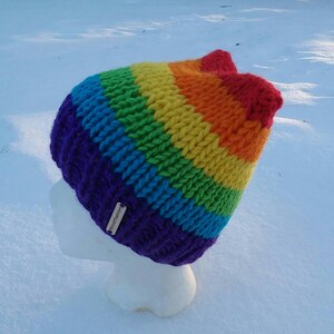 May include: A rainbow striped knitted hat with a purple brim and a small tag that says "Handmade".