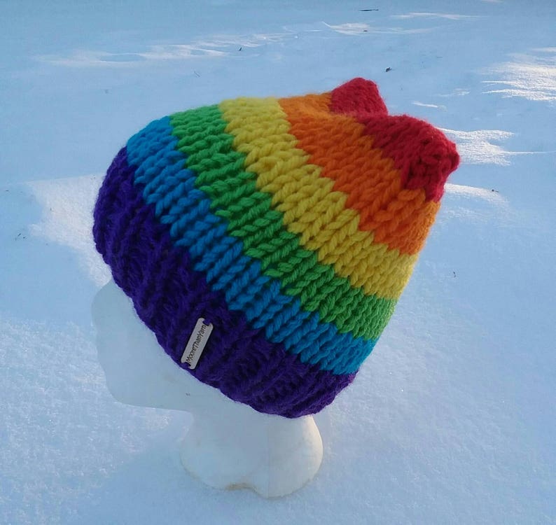 May include: A rainbow striped knitted hat with a purple brim and a small tag that says "Handmade".