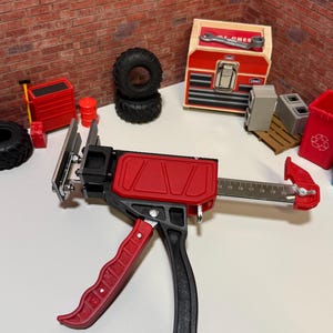 May include: A red and black trigger-operated clamp tool with a metal bar featuring a printed scale from 14 to 20 inches. The tool has a red handle, a red body casing, and a silver metal clamping head. It is positioned horizontally on a white surface.