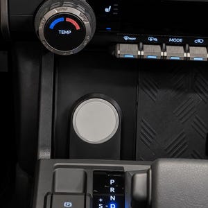 May include: A vehicle centre console featuring a circular temperature control dial with blue and red indicators, a gear shift lever, and a vertical display showing P, R, N, D, and S settings. Below are buttons for parking brake, hold, 4L, 4H, 2H, and a tow dial.