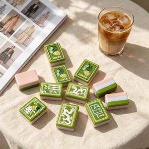 May include: A set of rectangular mahjong tiles featuring green and white designs, including two tiles labeled JOKER, one with a dragon, one with a peacock, one with the word EAST and an arrow, and several plain tiles with pink and green stripes.