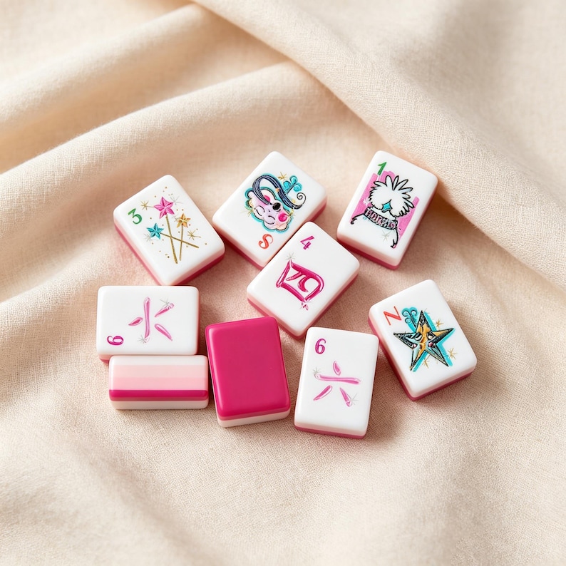 May include: A collection of nine rectangular mahjong tiles with white faces and magenta backs. The tiles feature various colorful illustrations including stars, a stylized character, and Chinese numerals in pink and teal ink on the white surfaces.