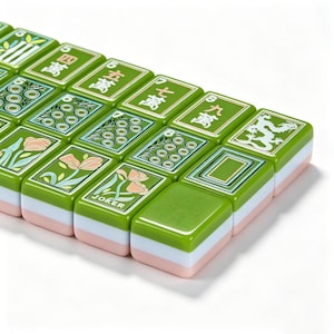 May include: A collection of rectangular Mahjong tiles featuring a green top surface with various engraved designs, including Chinese characters, floral patterns, a dragon, and the word JOKER. Each tile has a layered construction with green, white, and pink sides.