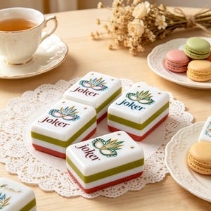 May include: Four rectangular mahjong tiles featuring a white top surface with a colorful mask illustration and the word joker printed in dark text. Each tile has a layered design with a white top, a green middle section, and a red base.