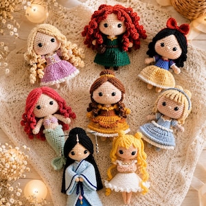 Pode incluir: Uma coleção de oito bonecas de crochê representando vários personagens com cores de cabelo e trajes distintos, incluindo uma sereia, uma figura em um quimono azul e outras em vestidos coloridos, dispostas sobre um tecido de renda branca.