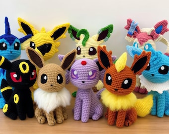 May include: A collection of nine handmade crochet plush toys representing various fictional creatures. The figures feature diverse colors including black, yellow, brown, purple, and blue, with distinct ear shapes, fluffy neck ruffs, and embroidered eyes.