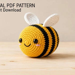 May include: A round, crocheted bee toy with yellow and black horizontal stripes, white wings, black safety eyes, and a stitched smile with pink blush marks. The text DIGITAL PDF PATTERN Instant Download is visible in the upper left corner.