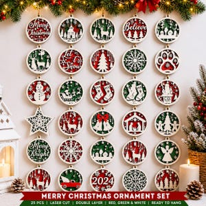 May include: A set of 25 laser-cut wooden Christmas ornaments featuring circular designs with red and green layered backgrounds. The ornaments display various holiday motifs including reindeer, snowflakes, stockings, bells, and the text Merry Christmas, Believe, Let it Snow, Merry & Bright, and 2024.