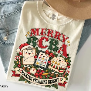 May include: An ivory t-shirt featuring a festive graphic with the text MERRY BCBA and MAKING PROGRESS BRIGHT. The design includes cartoon characters of a clipboard, a tablet, and a rating scale, all decorated with Christmas elements.