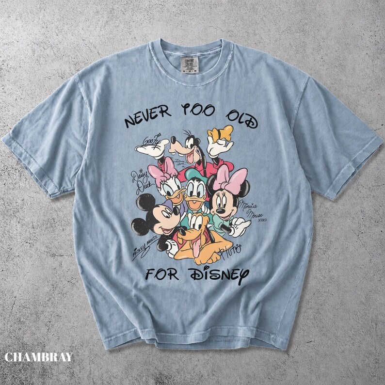 May include: A light blue short-sleeve t-shirt featuring a graphic print of Disney characters including Mickey Mouse, Minnie Mouse, Goofy, Daisy Duck, and Pluto. The text reads NEVER TOO OLD FOR DISNEY, with individual character names written in script.