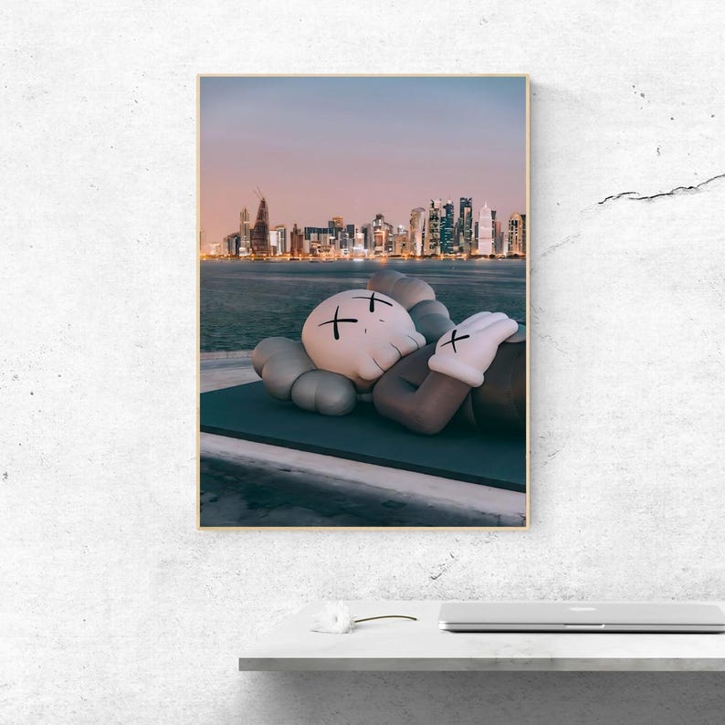 May include: A rectangular wall art print featuring a light-colored cartoon character with X-shaped eyes resting on a dark platform. In the background, a city skyline is visible across a body of water under a soft, gradient sunset sky.