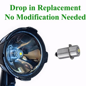 May include: A close-up of a black flashlight with a bright white LED bulb. The image also shows a replacement LED bulb, which is a small, silver-colored component with a white LED bulb. The text "Drop in Replacement No Modification Needed" is displayed above the image.