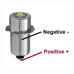 May include: A silver LED light bulb with a small, round, yellow LED light at the top. The bulb has a metal ring around the base and a small, round, black contact point at the bottom. The words "Negative -" and "Positive +" are written on the image.