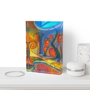 May include: A rectangular acrylic block featuring a vibrant, surreal illustration of a landscape with glowing orange orbs, twisted dark trees, and a textured yellow ground. The artwork displays a deep blue sky and a prominent orange spiral shape.