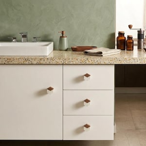 Puede incluir: Un mueble de baño blanco con cuatro pomos hexagonales de diseño bicolor en madera y mármol blanco. El mueble incluye una puerta y tres cajones apilados, rematado con una encimera moteada y un lavabo rectangular de color blanco.