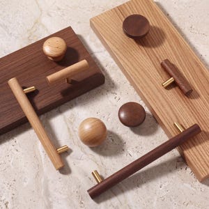 May include: A collection of wooden cabinet hardware including round knobs, T-shaped pulls, and long bar handles in light and dark wood tones. Each piece features brass-coloured metal mounting hardware attached to rectangular wooden display boards.