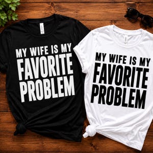 Peut inclure: Un t-shirt noir avec du texte blanc et un t-shirt blanc avec du texte noir, tous deux portant la phrase MY WIFE IS MY FAVORITE PROBLEM dans une police sans empattement grasse. Les t-shirts ont des manches courtes et un col rond.