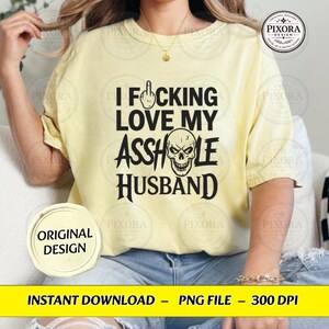 May include: A pale yellow short-sleeve t-shirt featuring black text that reads I FUCKING LOVE MY ASSHOLE HUSBAND, with a middle finger icon replacing the letter U and a skull illustration replacing the letter O in the word ASSHOLE.