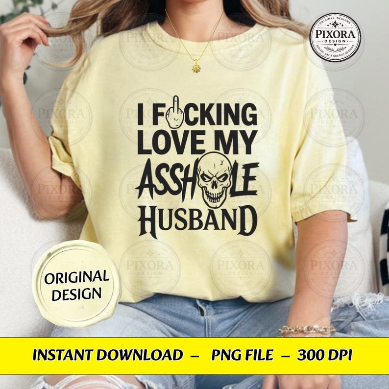 May include: A pale yellow short-sleeve t-shirt featuring black text that reads I FUCKING LOVE MY ASSHOLE HUSBAND, with a middle finger icon replacing the letter U and a skull illustration replacing the letter O in the word ASSHOLE.