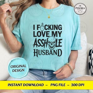 May include: A light blue t-shirt featuring black text that reads I F*CKING LOVE MY ASSHOLE HUSBAND, with a middle finger icon replacing the letter U in F*CKING and a skull graphic replacing the letter O in ASSHOLE.
