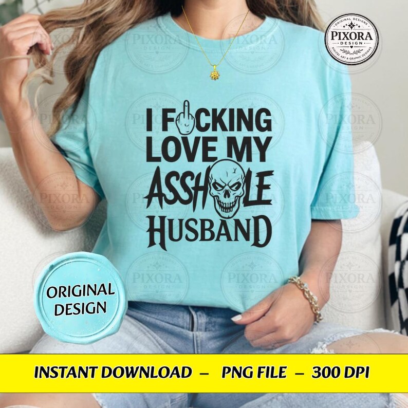 May include: A light blue t-shirt featuring black text that reads I F*CKING LOVE MY ASSHOLE HUSBAND, with a middle finger icon replacing the letter U in F*CKING and a skull graphic replacing the letter O in ASSHOLE.